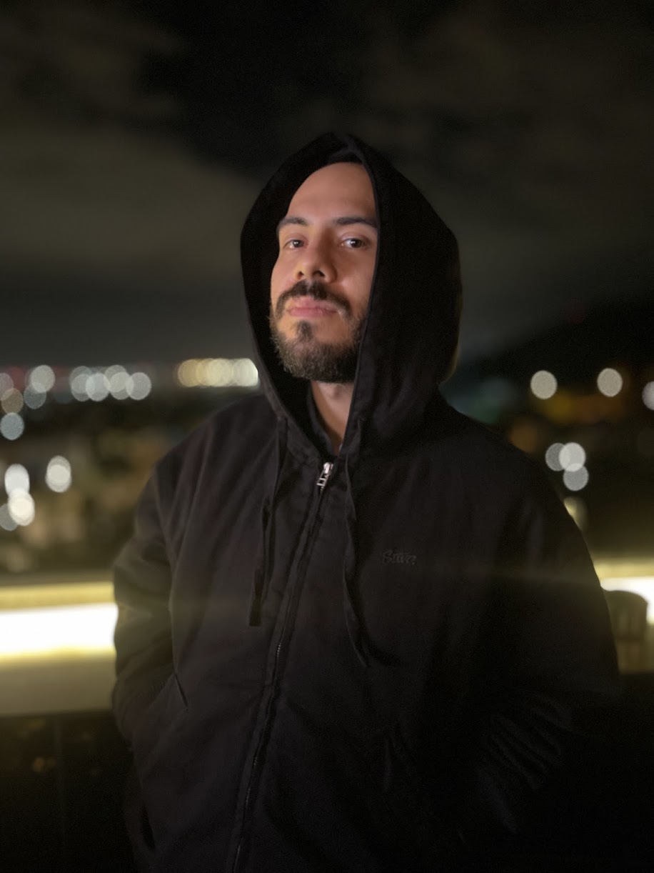 Portrait of Vallra, hooded, against Barcelona night lights